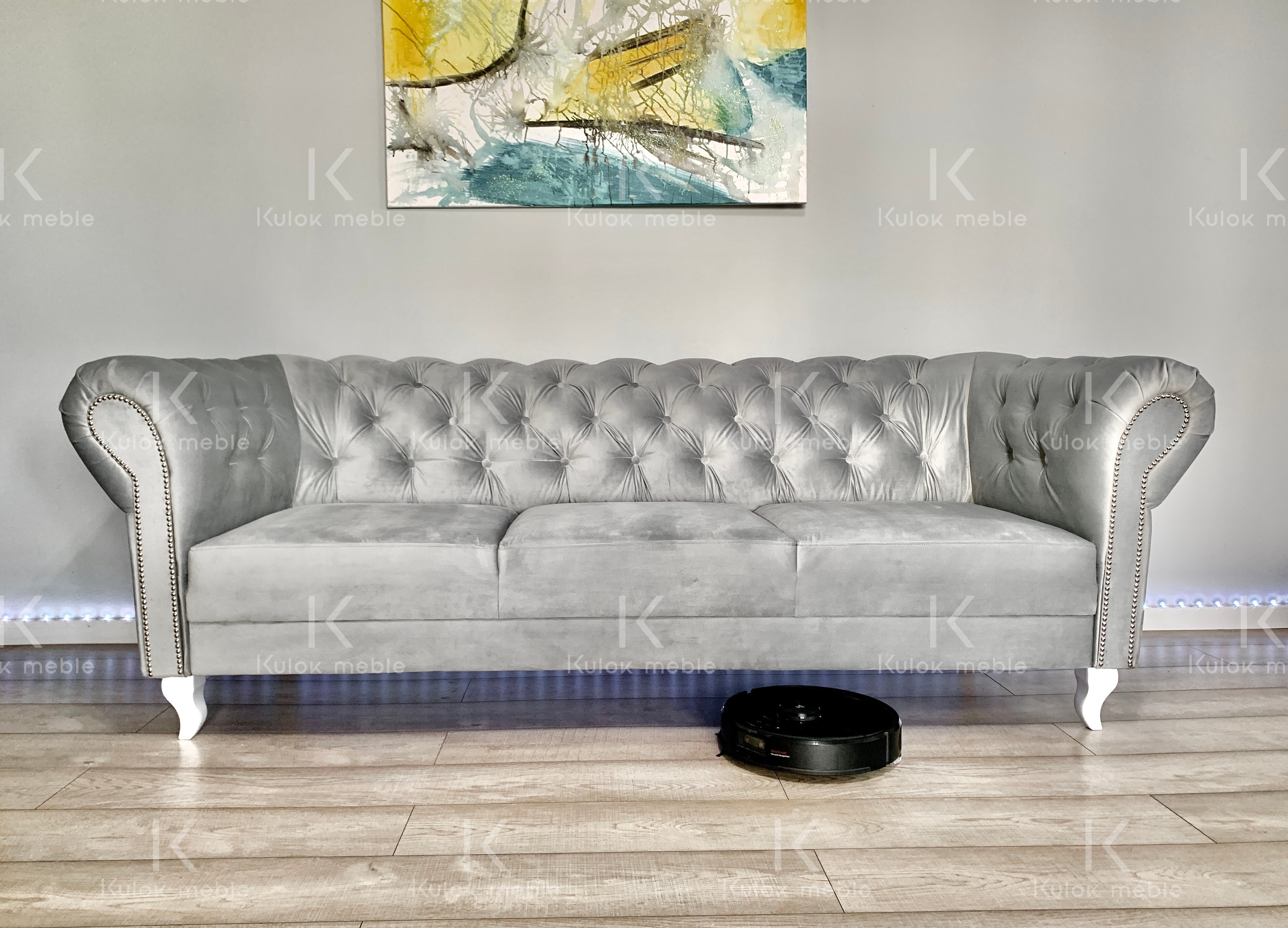 Szara sofa pikowana klasyczna do salonu  wysokie białe nogi.